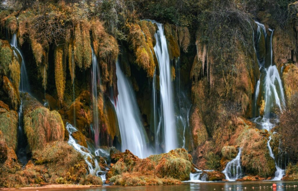 Capture the breathtaking beauty of Kravica Waterfalls in autumn, set in Bosnia's lush landscape.