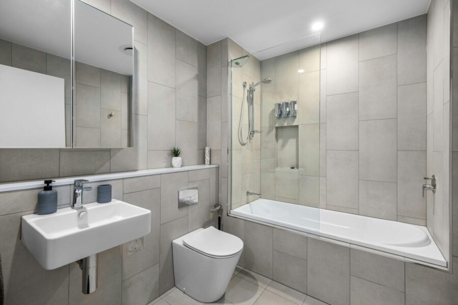 Sleek bathroom featuring gray tiles, white bathtub, and minimalist fixtures for a contemporary look.
