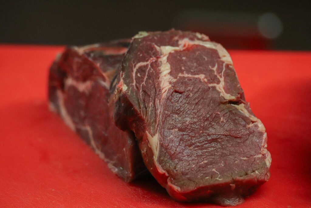 High-quality raw beef steak on a vibrant red cutting board, ready for cooking preparation.