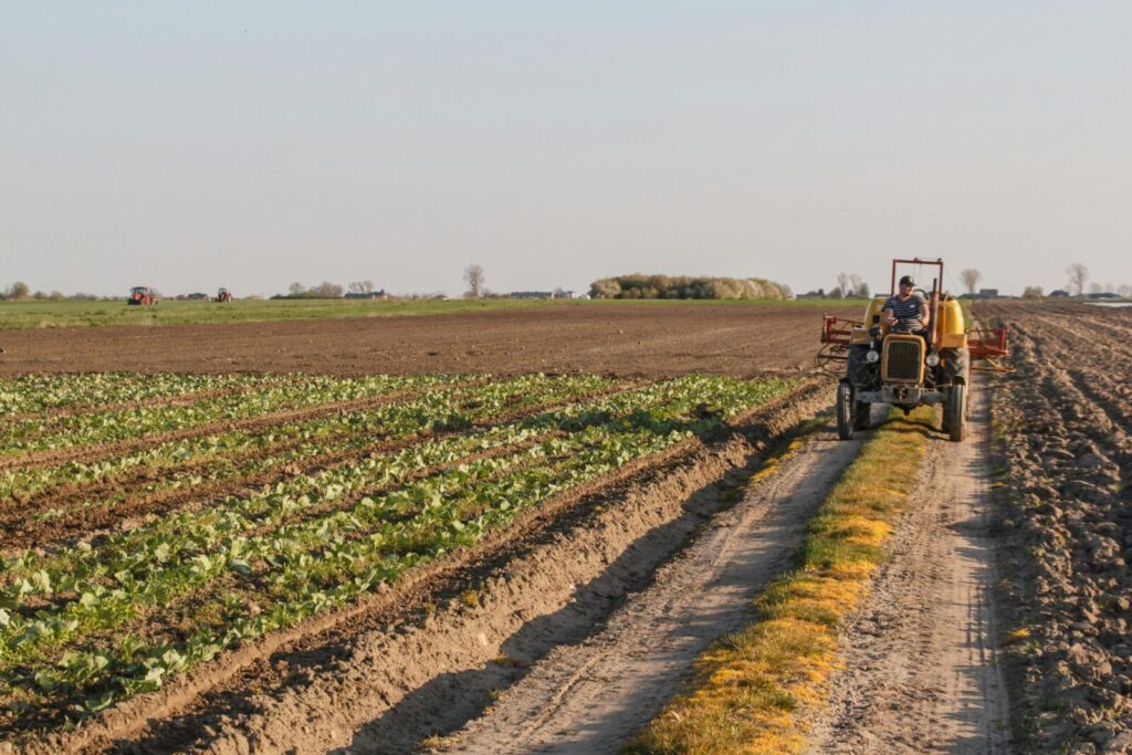 A tractor operates on a rural farm, plowing fields and maintaining crops under a clear sky.