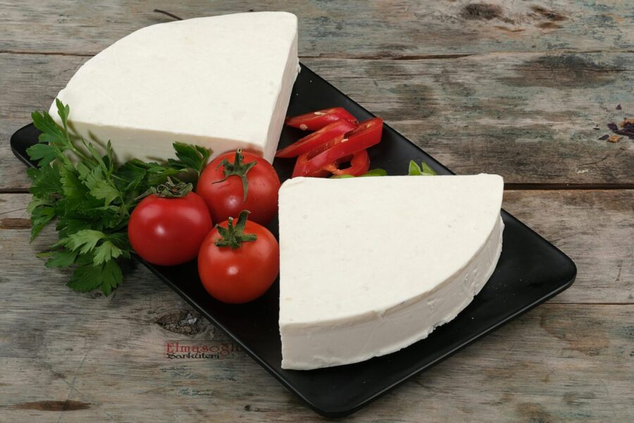 A still life of fresh white cheese with tomatoes and parsley on a rustic wooden table.