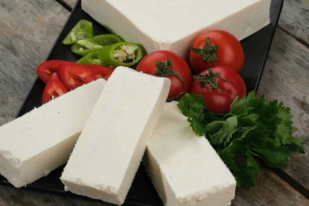 Assorted vegetables and white cheese on a wooden table, ideal for culinary themes.
