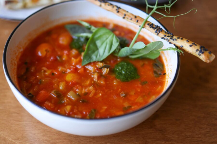 A vibrant tomato soup garnished with fresh herbs and a sesame breadstick, perfect for comfort food lovers.