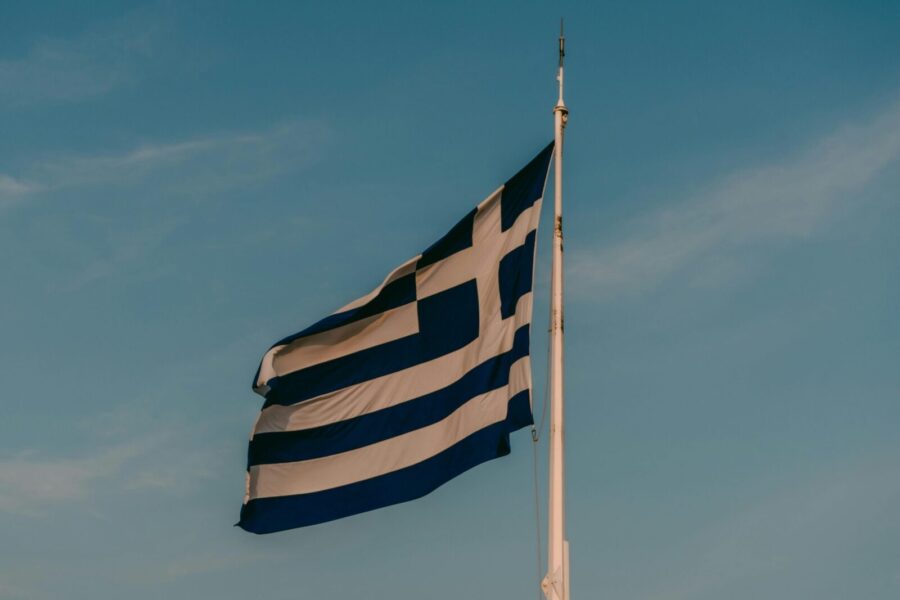 Vibrant Greek flag waving on a pole in Athens under a clear blue sky, displaying national pride.