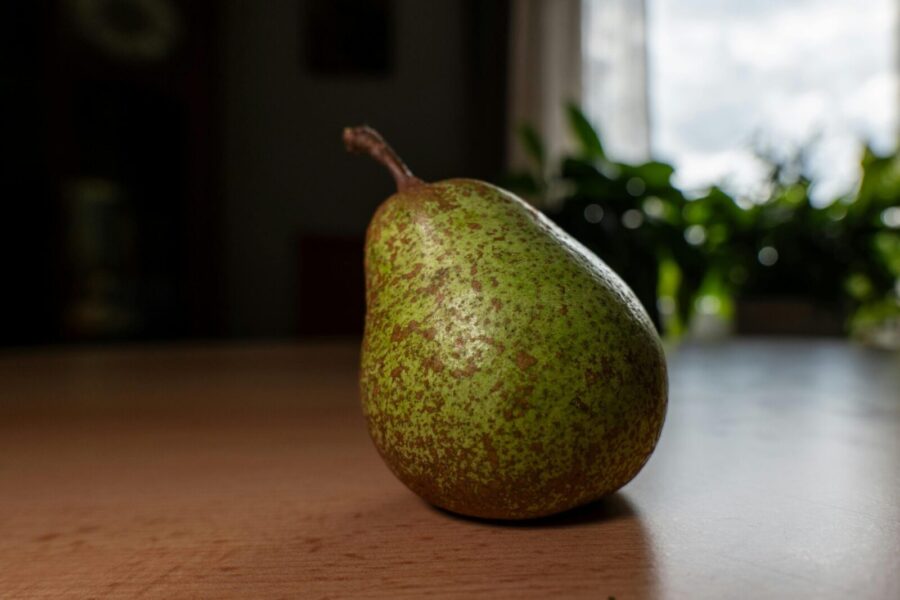 A close-up image of a ripe green pear placed on a wooden table with soft natural lighting.