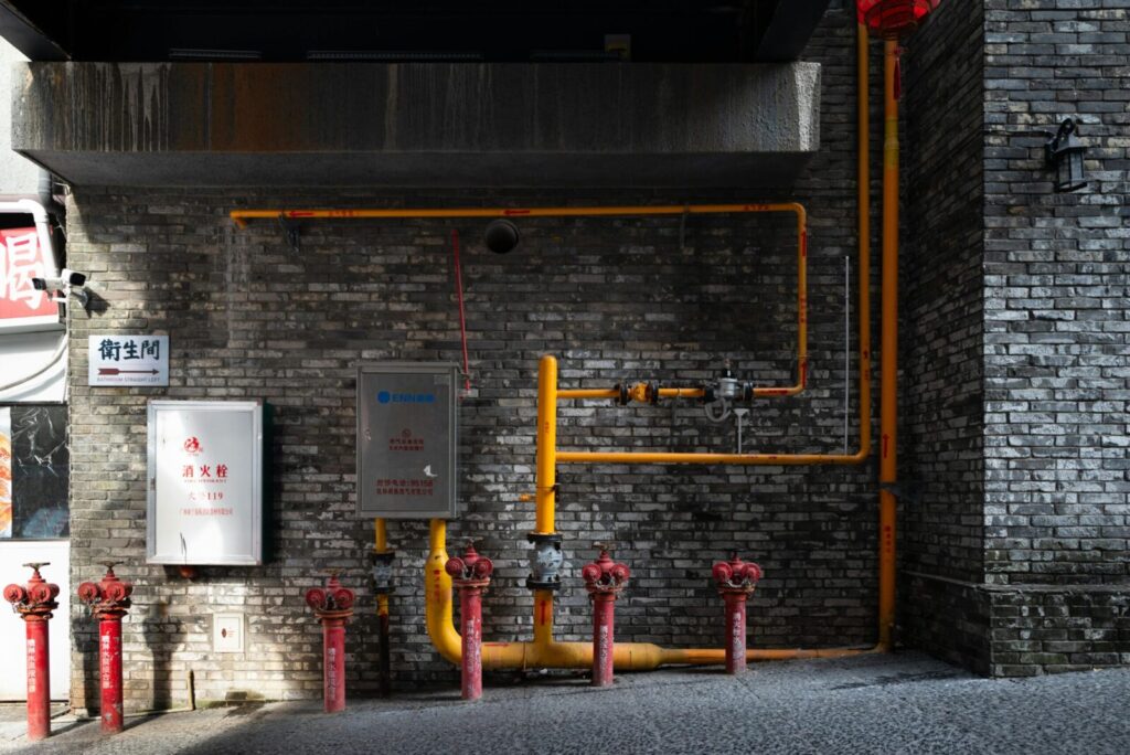 Brick wall with red hydrants and yellow piping in an urban alleyway setting.