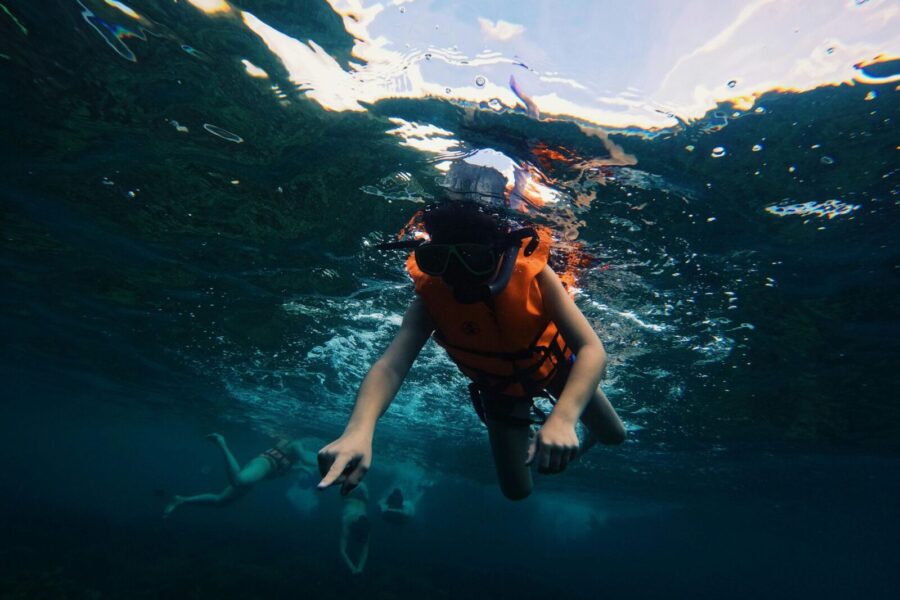 A child snorkeling in the clear blue waters of Satun, Thailand, wearing an orange life vest.