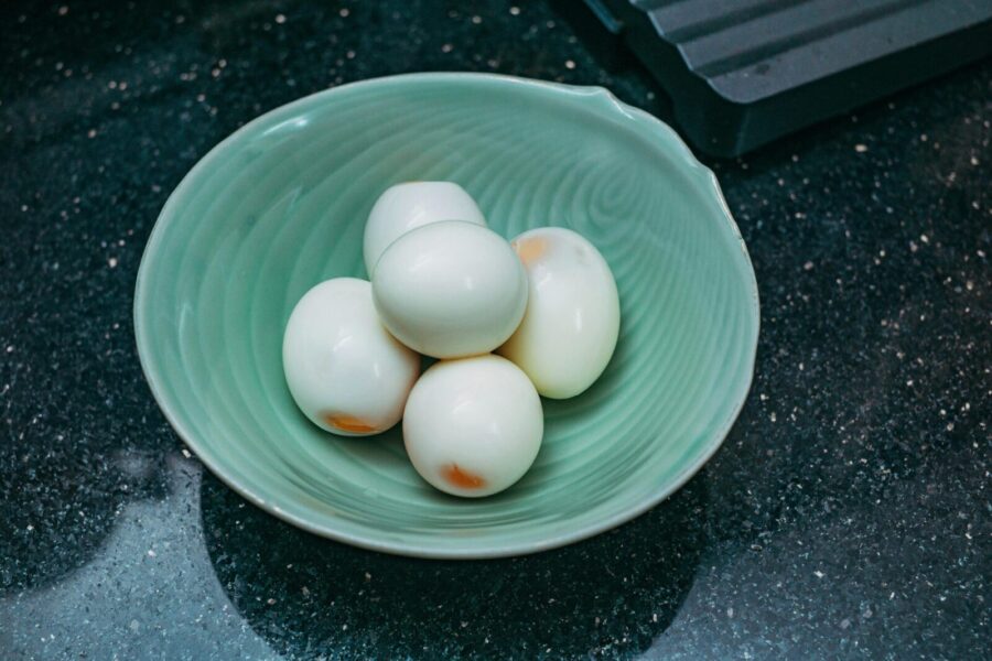 A top-down view of boiled eggs in a textured green bowl on a dark countertop.