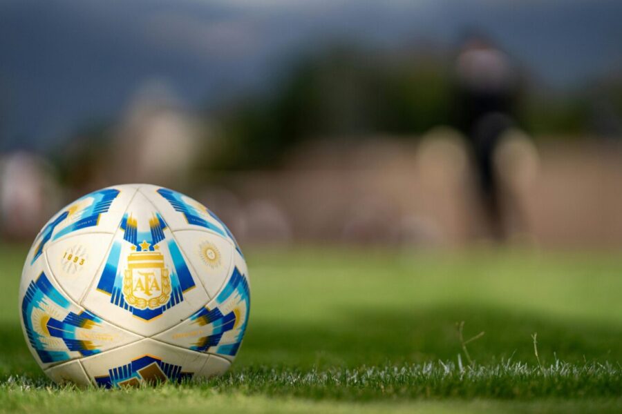 Close-up of an official Argentine soccer ball resting on a green field with a blurred background.