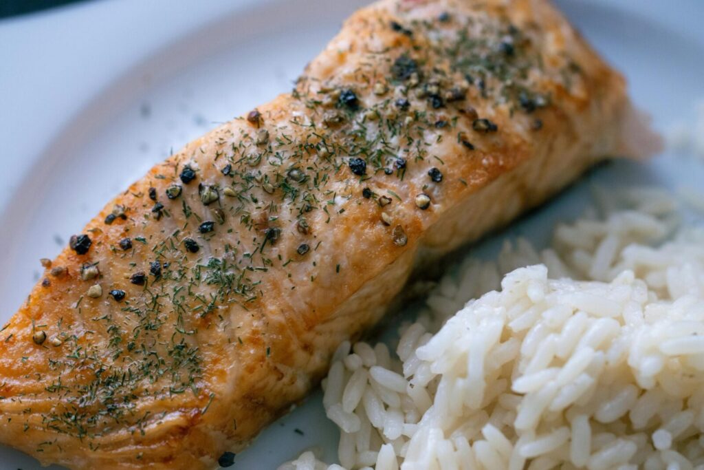 Grilled salmon fillet garnished with herbs and served with a side of steamed rice, perfect for a healthy meal.