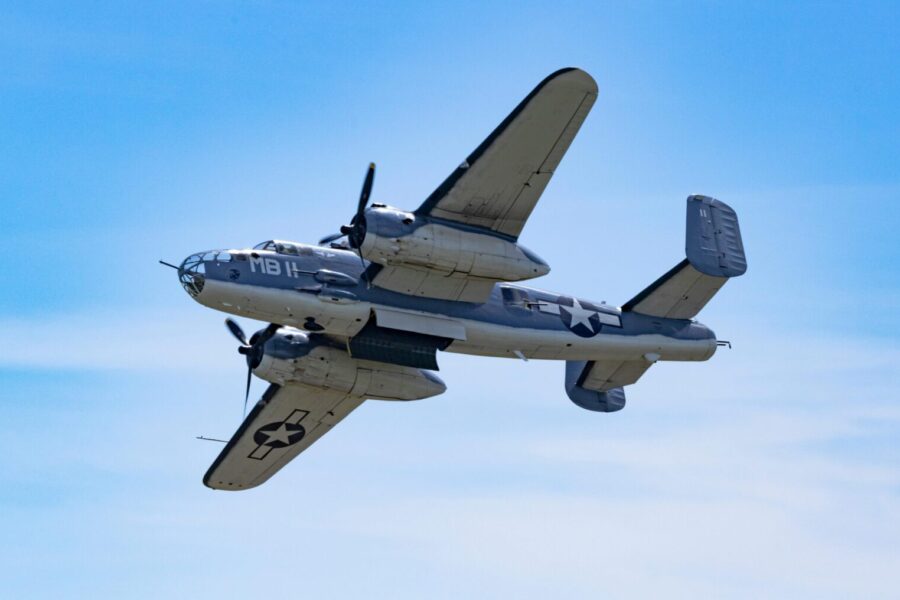 A vintage World War II B-25 Mitchell bomber flying under clear skies, showcasing historic aviation.