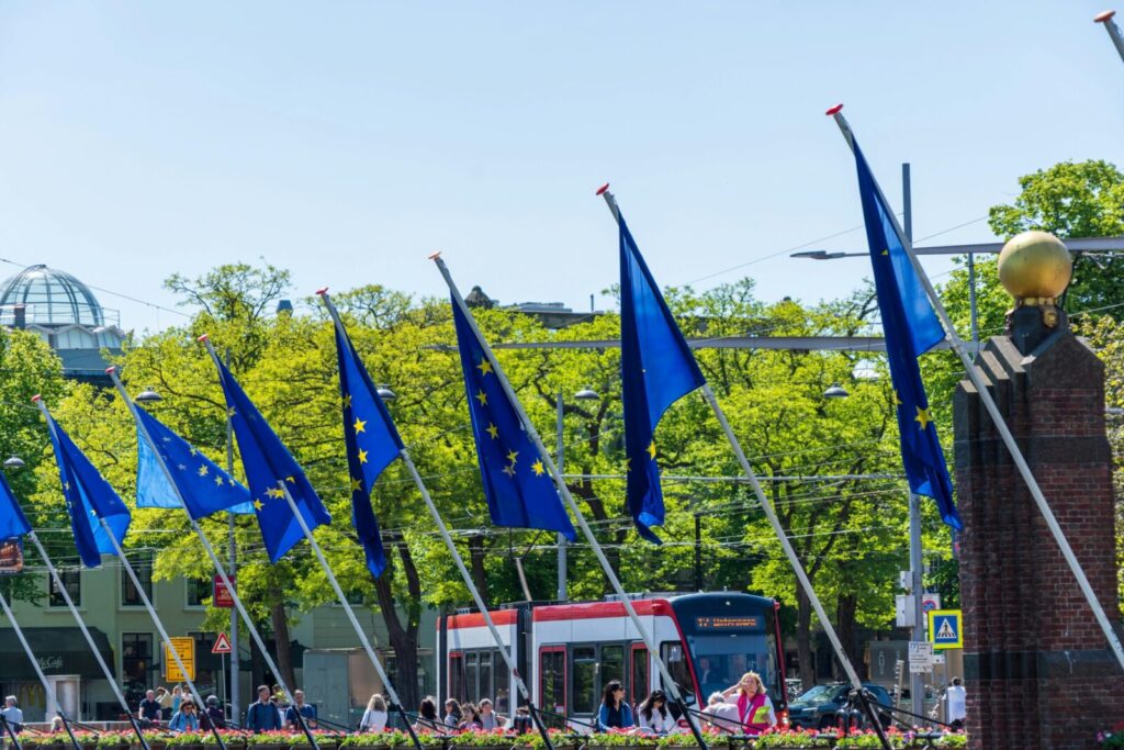 European Union flags displayed prominently in a vibrant city scene with tram and people.