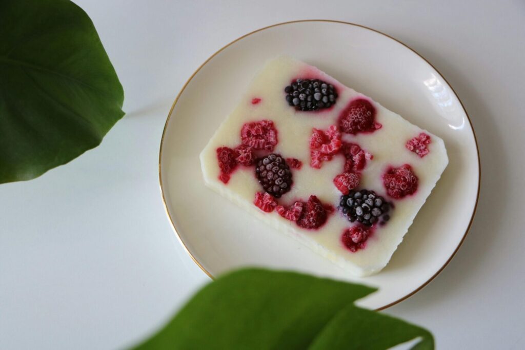 Frozen yogurt bar topped with raspberries and blackberries on a white plate, surrounded by leaves.