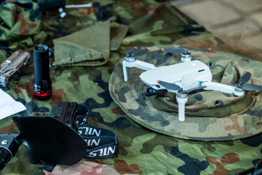Compact white drone on camouflage gear, surrounded by flashlight and tools.