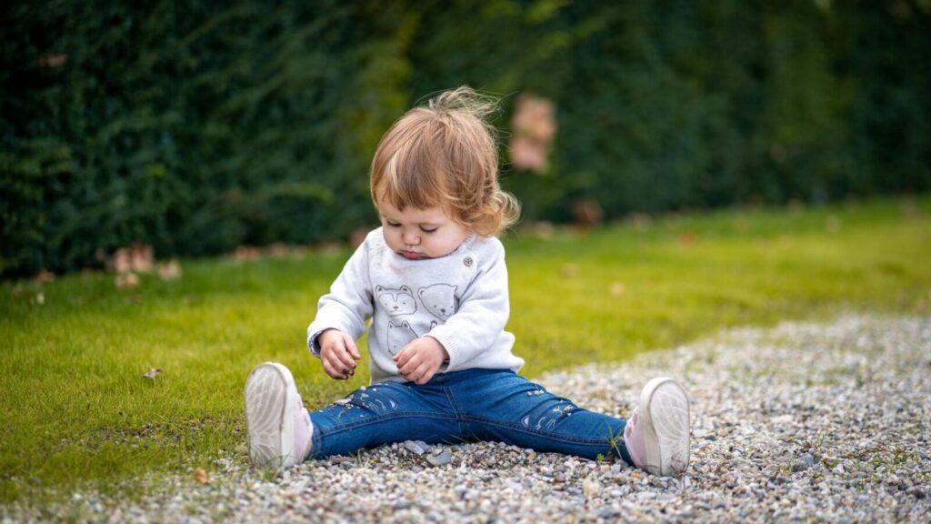 A cute toddler sitting on grass in Vienna enjoying playtime outdoors, showcasing childhood joy.