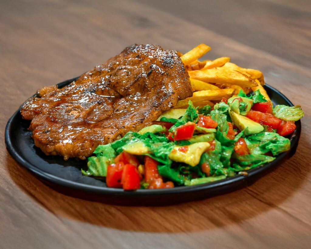 Juicy grilled steak served with crispy fries and a fresh green salad on a dark plate.
