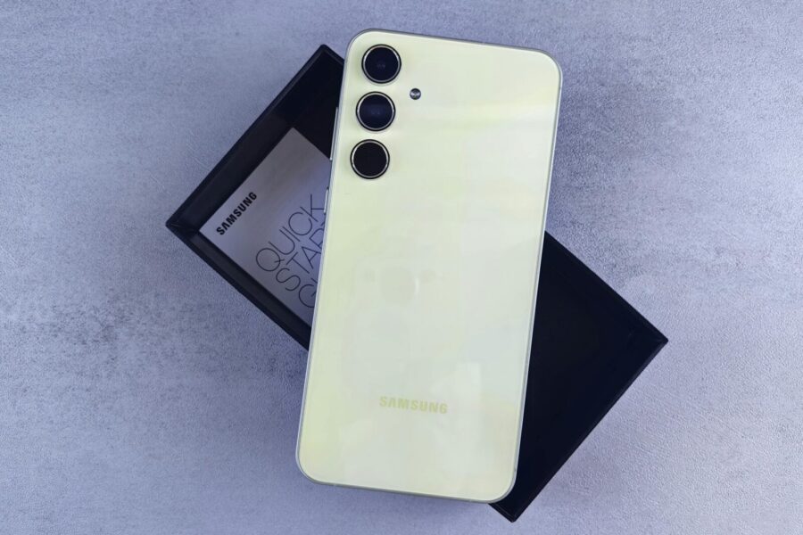 Yellow Samsung smartphone displayed on a gray surface with its box and quick start guide.