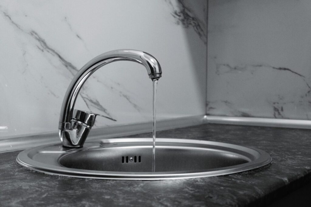 Chrome faucet with running water in a modern kitchen with marble countertop.