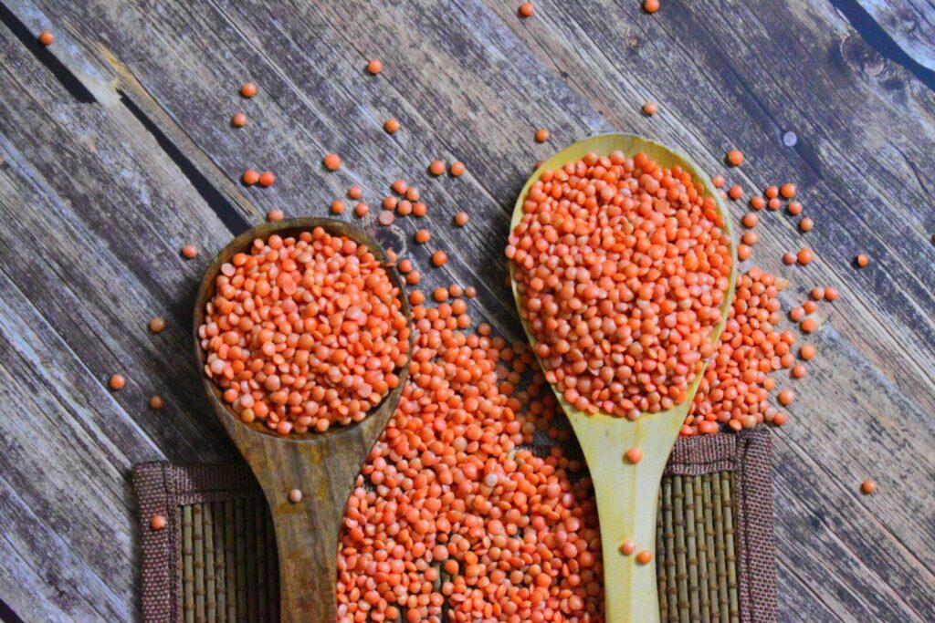 Two wooden spoons filled with vibrant red lentils on a rustic wooden surface.