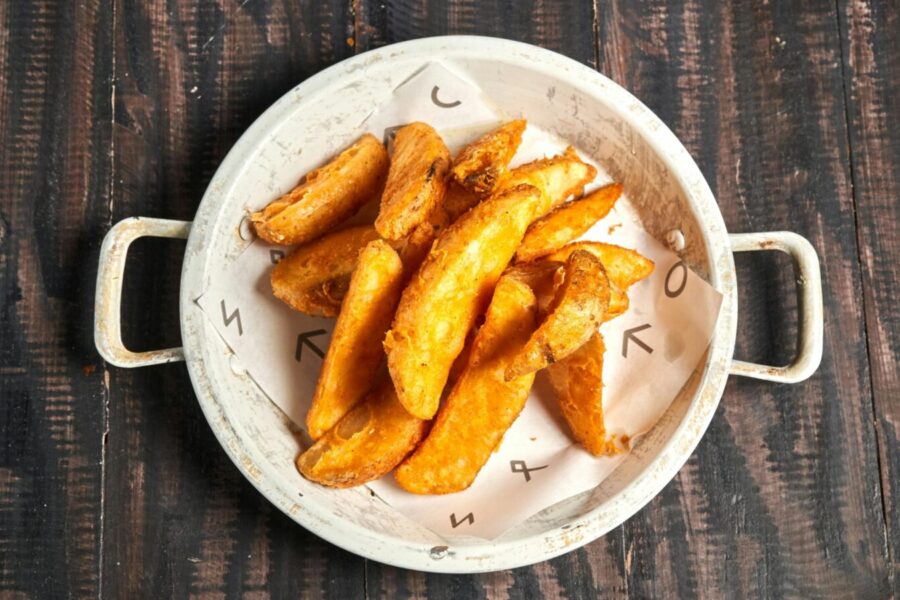Golden crispy potato wedges served in a rustic white bowl on wood.