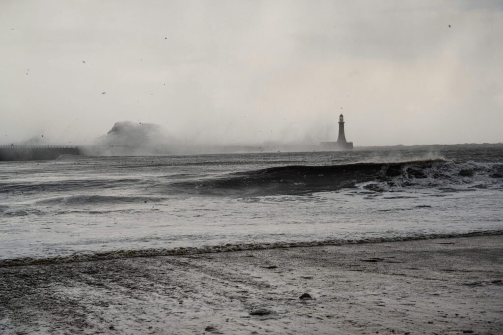 A stormy seascape with waves crashing near a distant lighthouse, conveying a sense of drama and isolation.