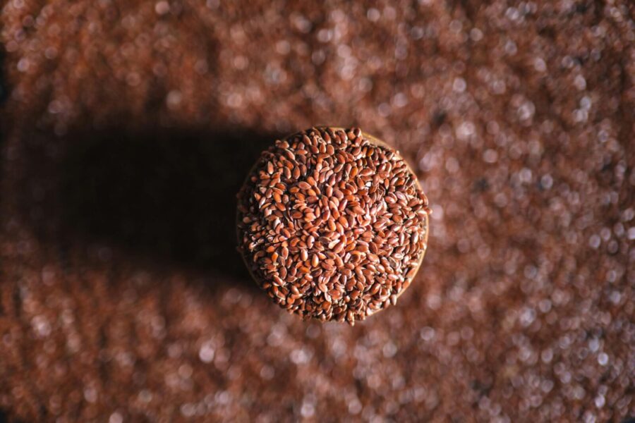 A top-down view of a jar filled with flax seeds, surrounded by scattered seeds on the surface.