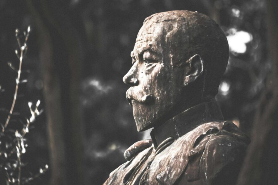 A dramatic monochrome photo of a bust sculpture outdoors, highlighting its weathered texture.