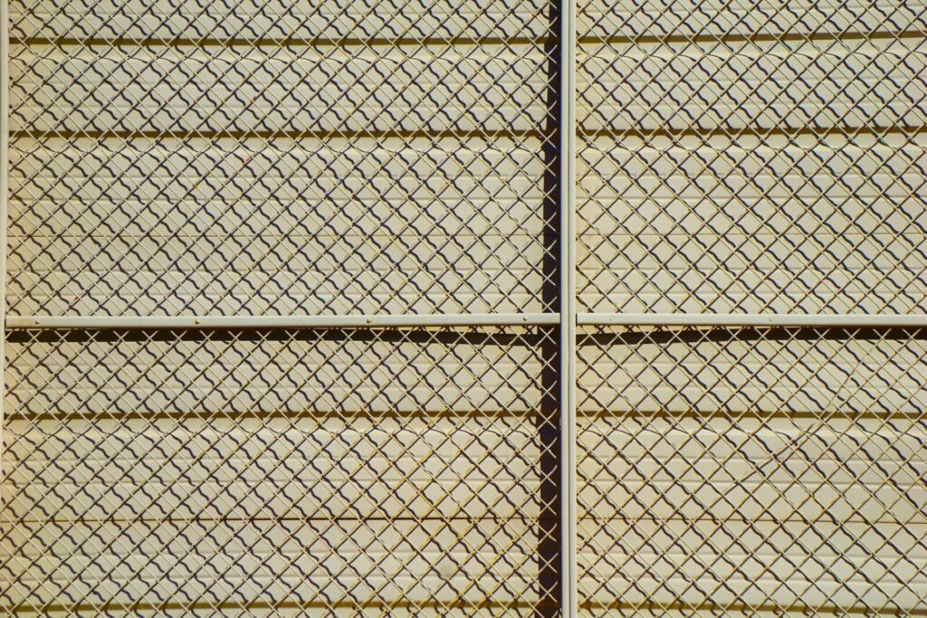 Detailed pattern of a chain-link fence casting shadows, creating a textured grid effect.
