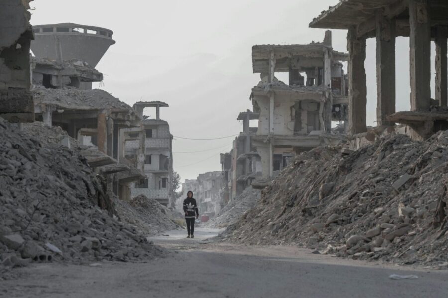 A solitary figure walks through the devastated ruins of Damascus, Syria, highlighting the aftermath of conflict.
