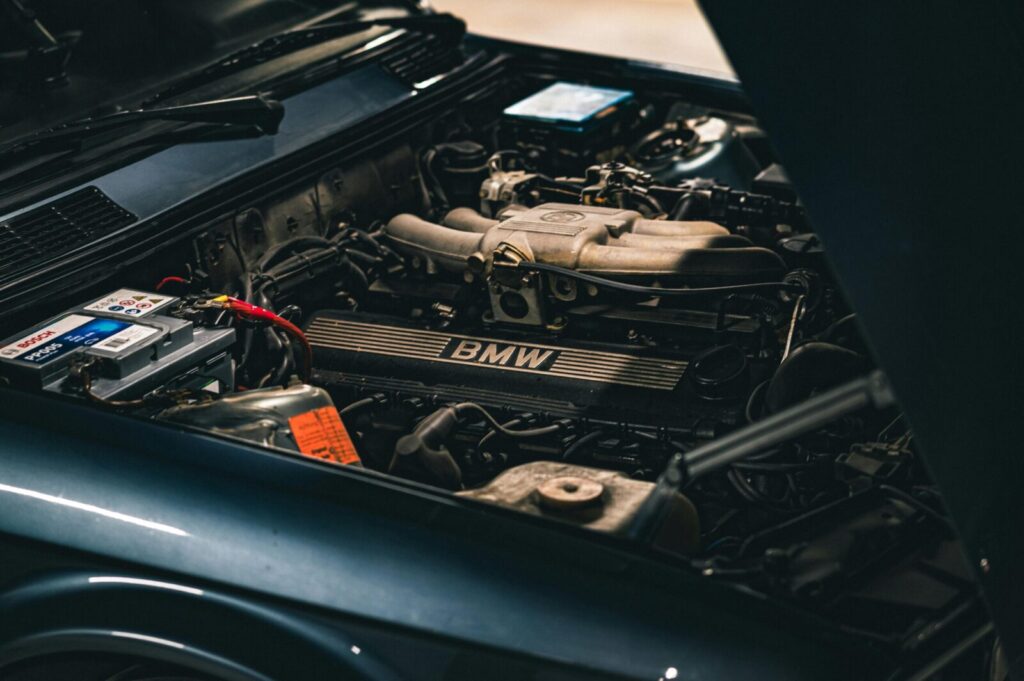 Detailed view of a BMW car engine with visible battery, showcasing mechanical intricacies in a dimly lit garage.