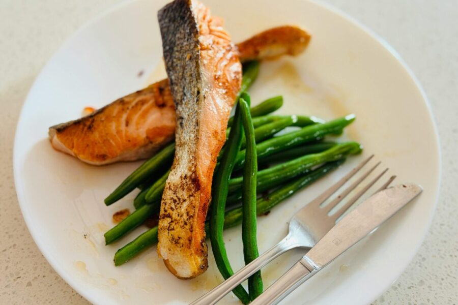 Delicious grilled salmon fillet served with fresh green beans on a white plate, perfect for a healthy meal.