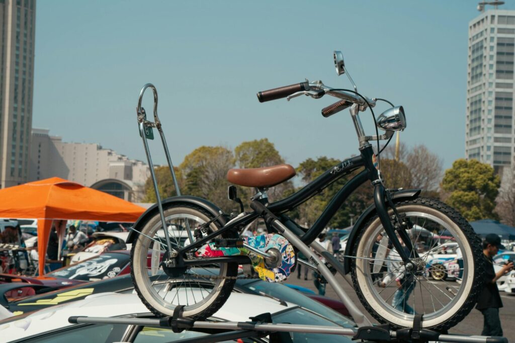 A vintage bicycle is mounted on a car roof at a vehicle exhibit in Tokyo, Japan, on a sunny day.