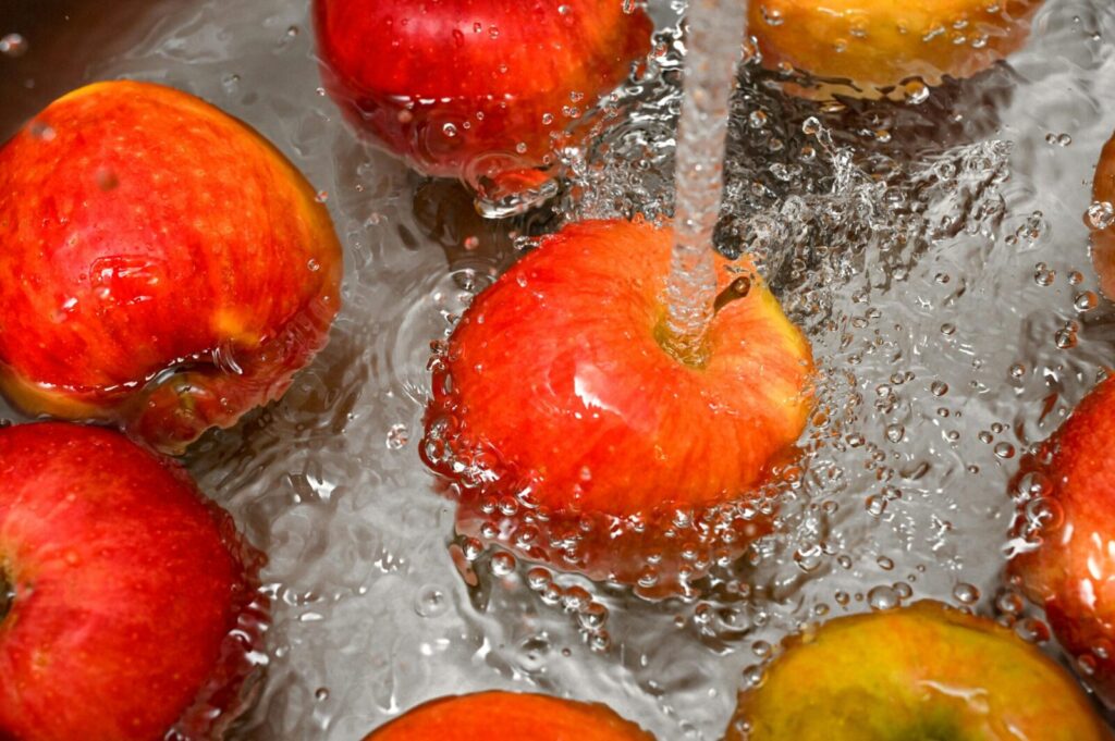 Vibrant red apples under a water stream, promoting cleanliness and freshness.
