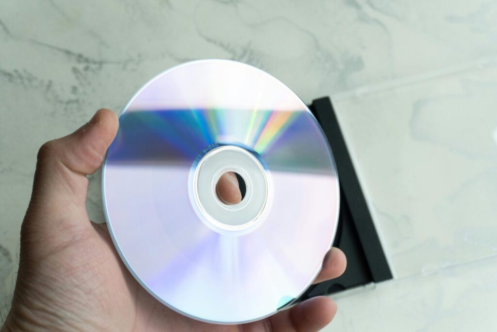 Close-up of a person holding a reflective CD disc with a transparent case on a marble background.