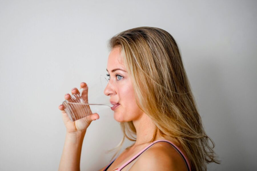 Side view of a woman with blonde hair drinking water from a clear glass.