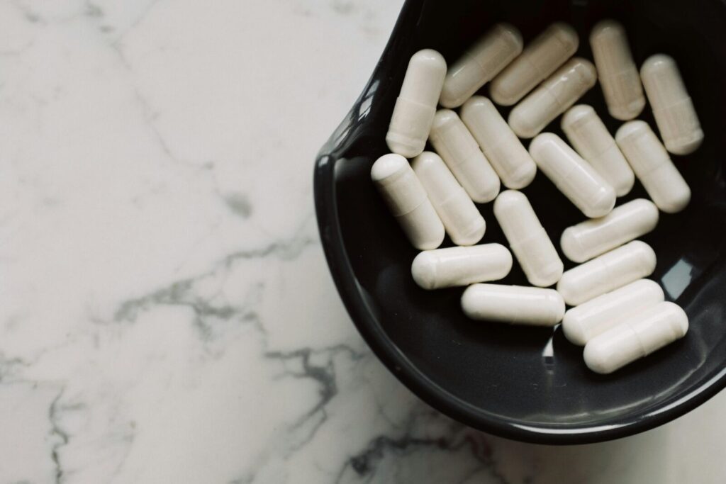 Close-up of white capsules in a black bowl on a marble surface, symbolizing healthcare and medication.
