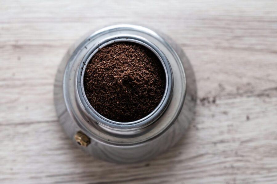 Top view of freshly ground coffee in a stainless steel container on a wooden surface.