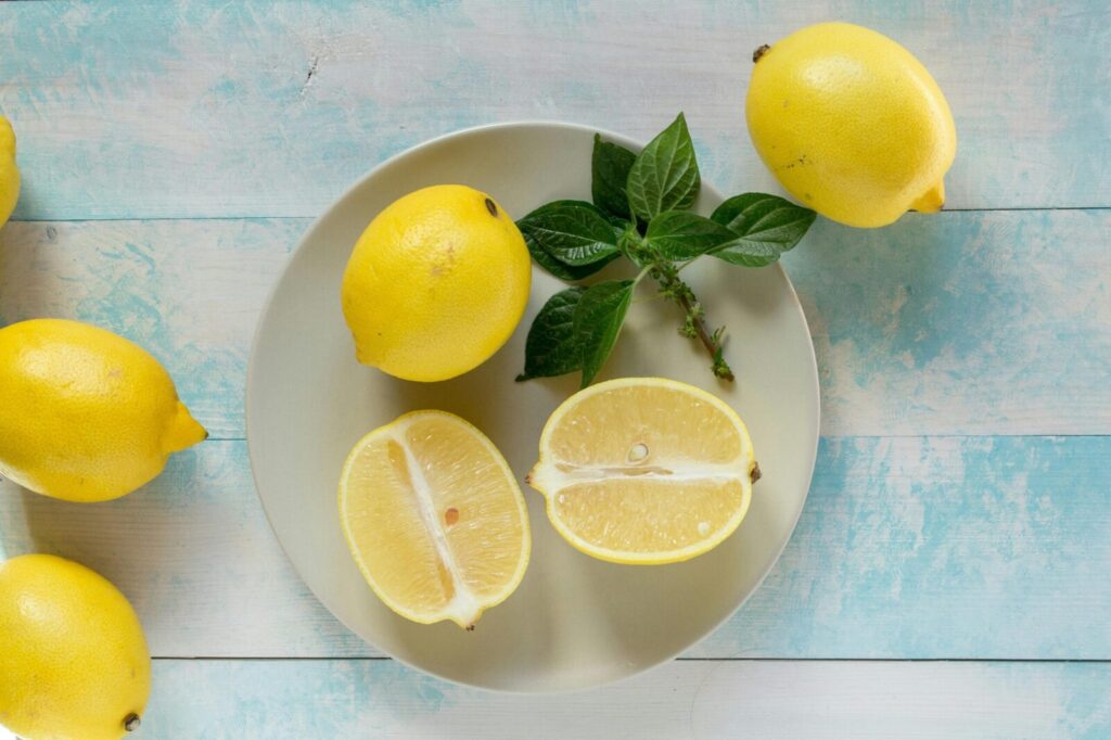 Top-down view of lemons with fresh green leaves on light wooden background.