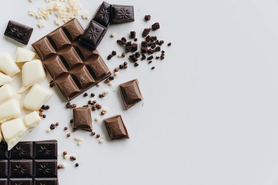 A flat lay of assorted milk, dark, and white chocolate bars and pieces on a white surface.