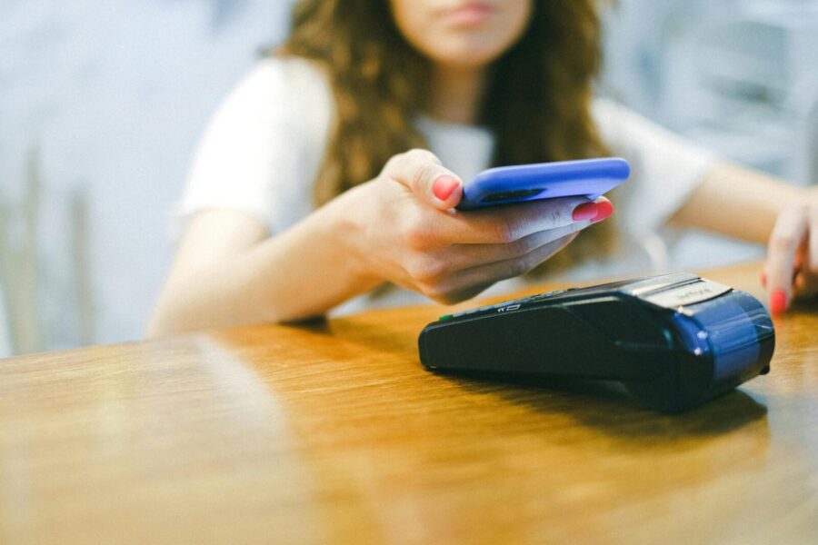 A woman processes a contactless payment using her smartphone at a payment terminal.