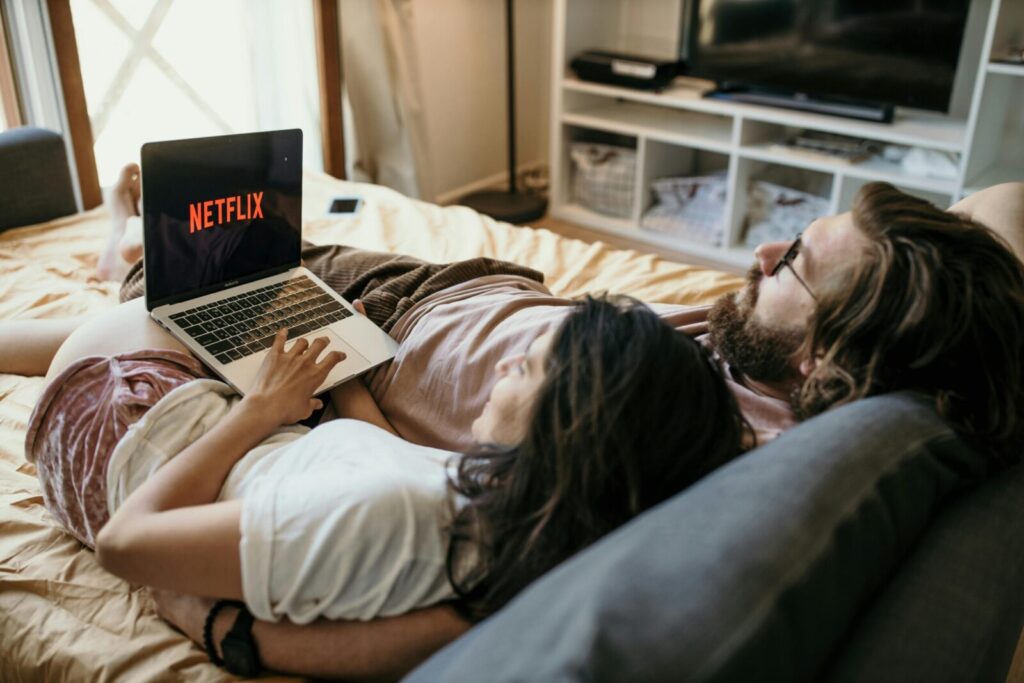 A cozy couple lounging in bed, streaming Netflix together on a laptop, enjoying a peaceful moment.