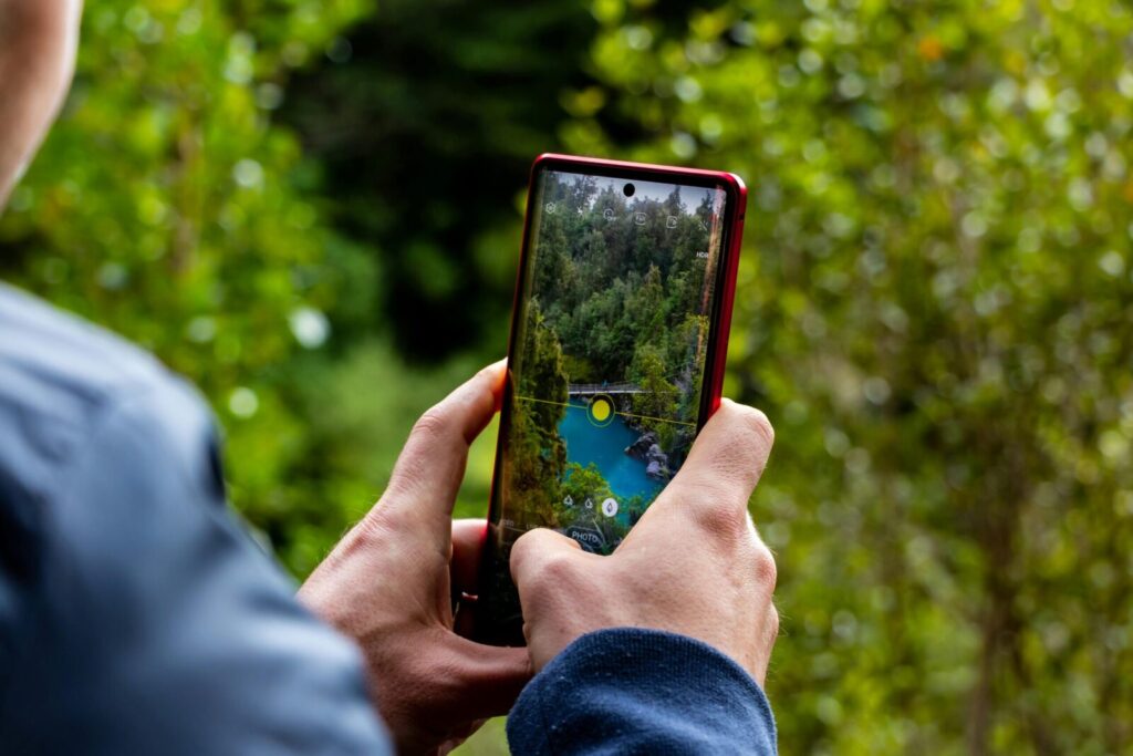 Hands holding a smartphone capturing a scenic river view with trees.