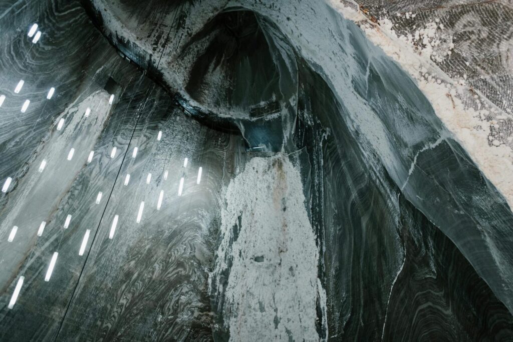 From above of hanging LED lamps and salty stalactites on uneven walls of Salina Turda mine in Romania