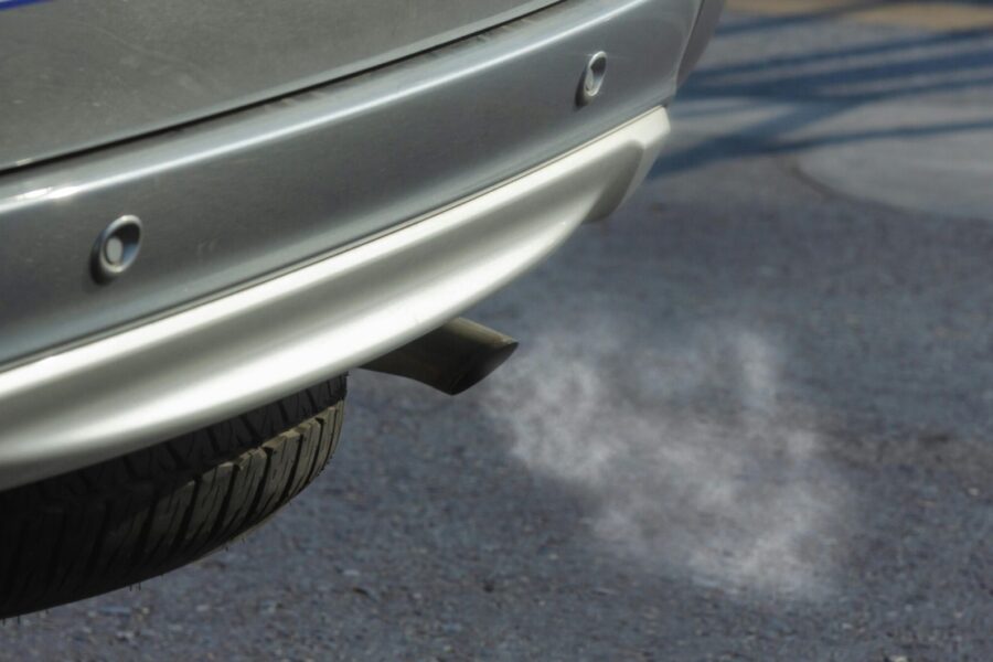 Close-up of a silver car exhaust pipe emitting smoke on asphalt road.