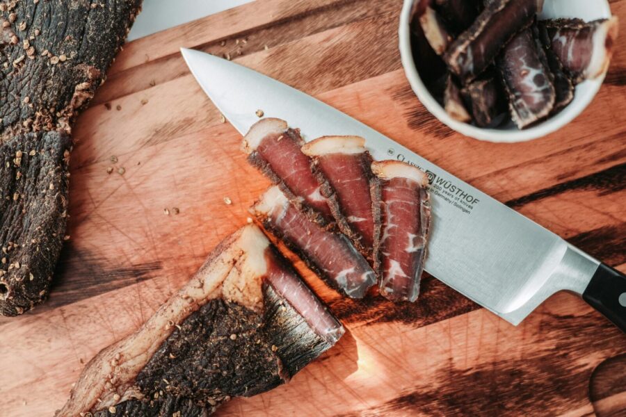 Delicious slices of cured meat displayed on a wooden board with knife in view, perfect for culinary presentations.
