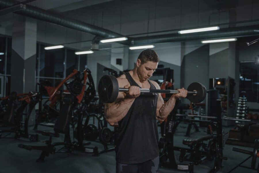 Muscular man intensely lifting a barbell in a well-equipped gym setting.