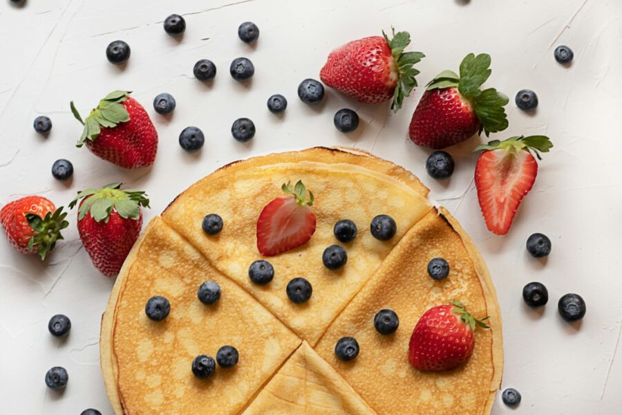 Mouth-watering crepes topped with fresh strawberries and blueberries on a white table.