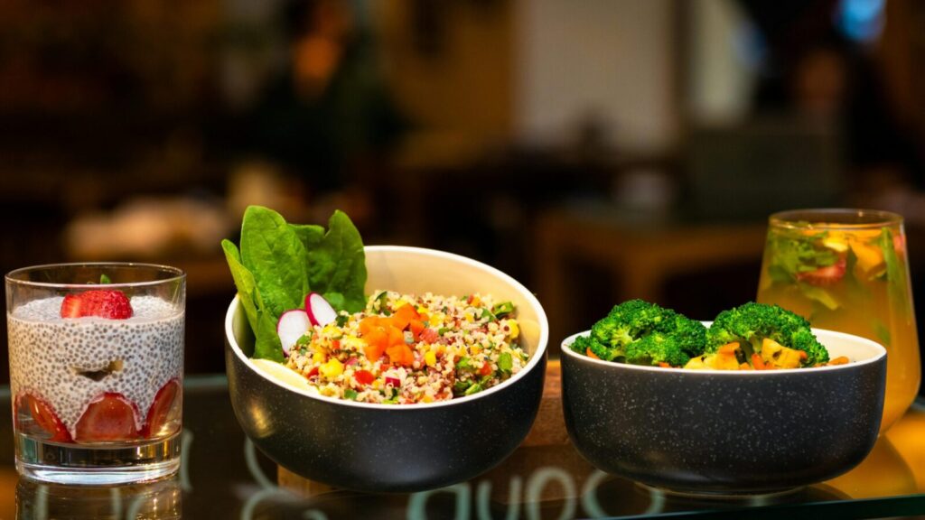 Delicious bowls of quinoa salad, broccoli, and chia pudding with refreshing drink.