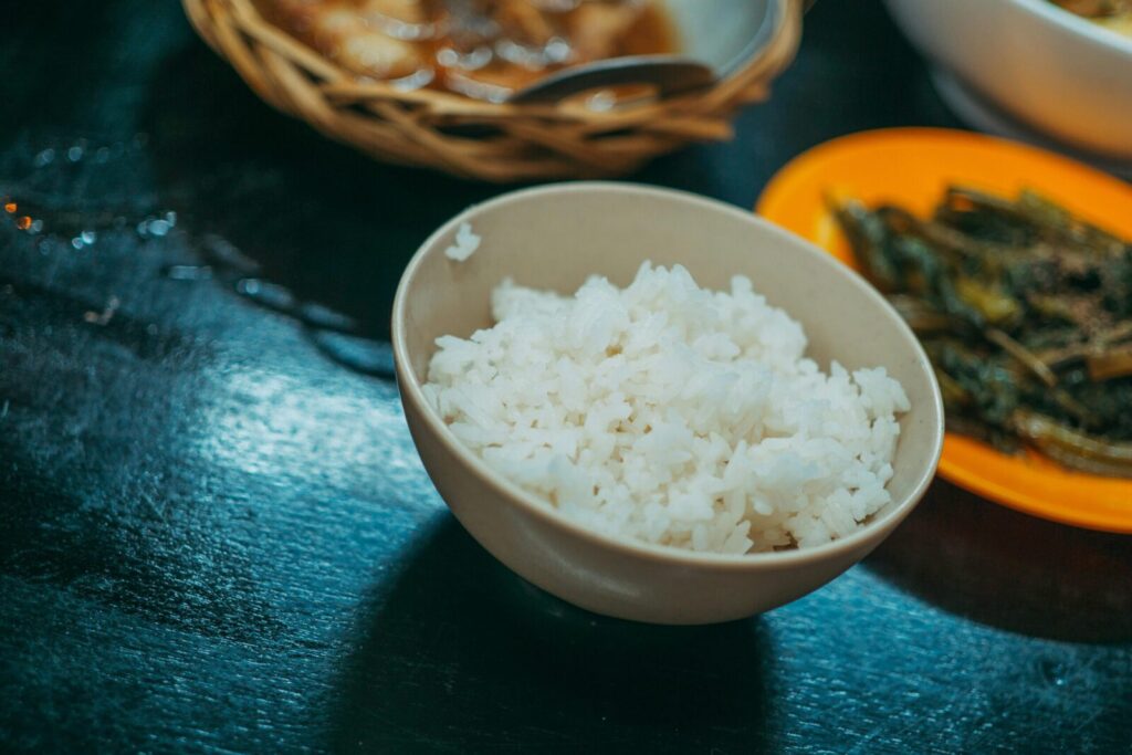 A close-up shot of a bowl of white rice with sautéed vegetables on the side, ideal for food blogs.