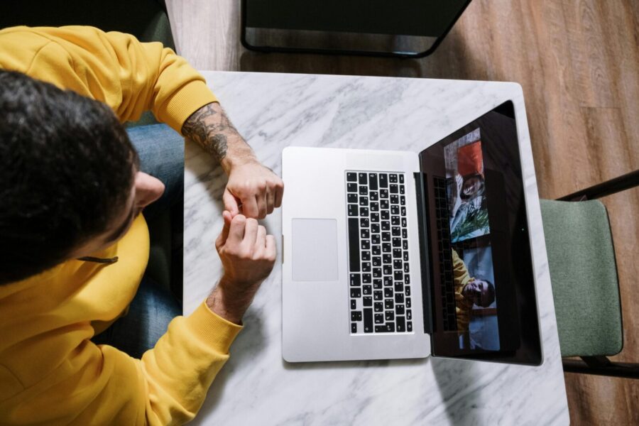Overhead view of man in yellow sweater video calling on laptop from a marble table.